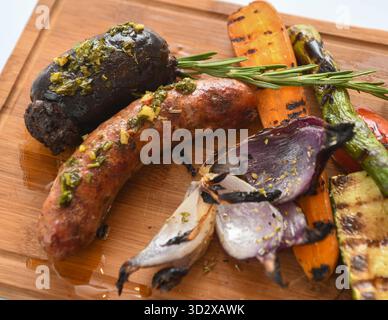 Salsicce grigliate con verdure grigliate su tagliere in legno. Foto Stock