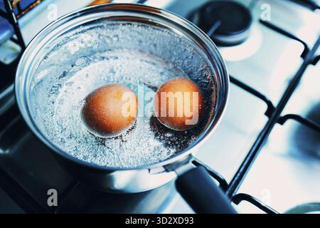 Pentola in acciaio inossidabile con due uova bollenti, colazione in acqua con vista dall'alto su una stufa a gas Foto Stock