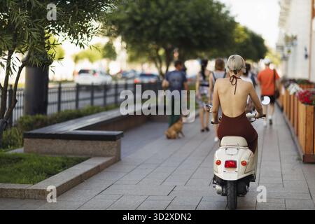 Giovane modella bionda che corre su moto scooter ciclomotore in città Foto Stock