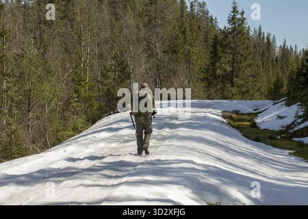 Scongelamento primaverile, scioglimento della neve, uomo con grande backpadk passeggiate lungo la strada innevata in primavera Foto Stock