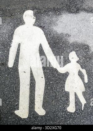Figura dipinta di bianco per adulti e bambini che camminano su una superficie asfaltata nera di un sentiero Foto Stock