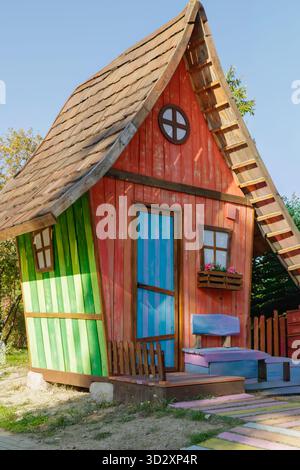 Una vivace casa di gioco in legno dipinta in rosso, verde e blu si erge in un giardino soleggiato. Con il suo tetto curvo e i dettagli affascinanti, crea un Foto Stock