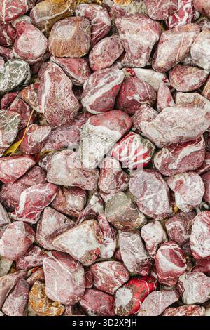 Primo piano di pietre di marmo rosse e bianche utilizzate per la decorazione del giardino. La consistenza liscia, i motivi naturali e i toni contrastanti creano un orn organico Foto Stock