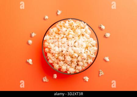 Disposizione piatta di smartphone con schermo bianco vuoto tenuto sopra la ciotola di popcorn su sfondo arancione, simboleggiando lo streaming moderno e il concetto di notte di film Foto Stock