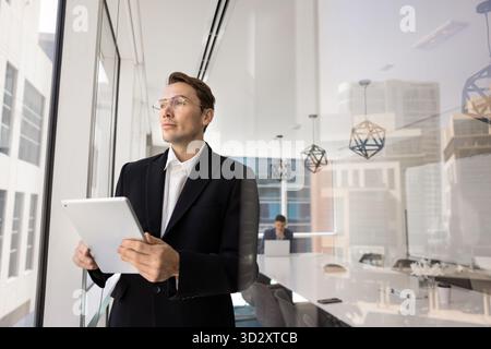 Dirigente aziendale serio e ambizioso nel settore dell'abbigliamento formale che tiene un tablet digitale Foto Stock