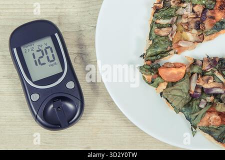 Glucometro con il risultato della misurazione del livello di zucchero e un pezzo di pizza vegetariana appena sfornata. Concetto di nutrizione durante il diabete Foto Stock