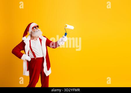 Funky Babbo Natale in abito rosso con un rullo di vernice su un vibrante sfondo giallo che trasmette divertimento e creatività festivi Foto Stock