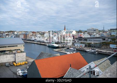 Haugesund, il porto norvegese con case colorate, barche e una guglia della chiesa sotto un cielo nuvoloso Foto Stock