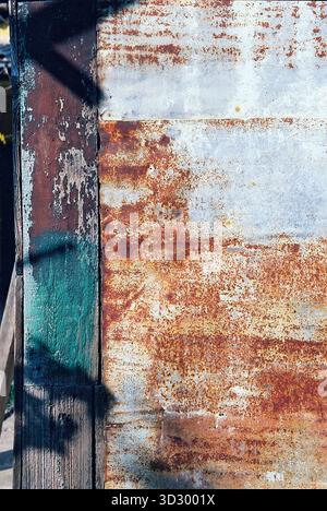 Tetto rivestito in lamiera con consistenza robusta, parzialmente arrugginito e parzialmente verniciato di verde, illuminato dal sole e catturato in calde tonalità analogiche. Foto Stock