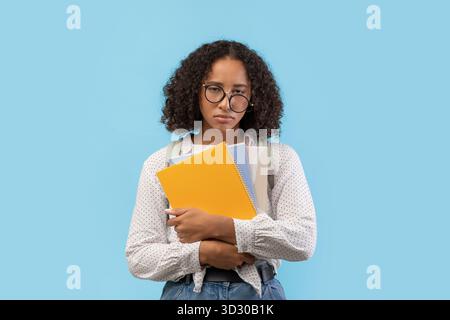 La studentessa Nera stanca si prepara agli esami universitari mentre tiene i notebook in Blue Studio Foto Stock