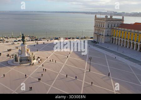 Ampia vista della Piazza del Comércio di Lisbona con la statua del re José i, la passeggiata sul lungomare e la gente che cammina attraverso la piazza. Foto Stock