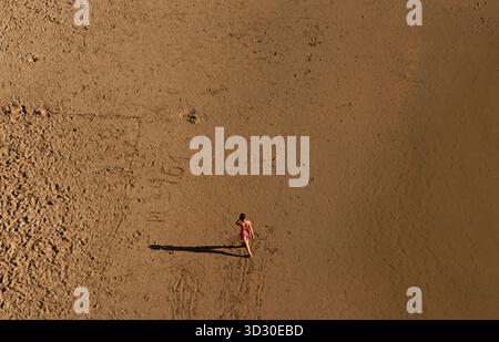 Donna solitaria che cammina attraverso l'ampia spiaggia sabbiosa di Alentejo, Portogallo, gettando una lunga ombra al sole del tardo pomeriggio. Foto Stock