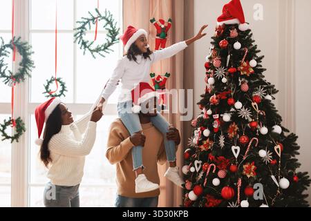 La famiglia Happy Black si diverte a decorare insieme l'albero di Natale nell'accogliente soggiorno Foto Stock