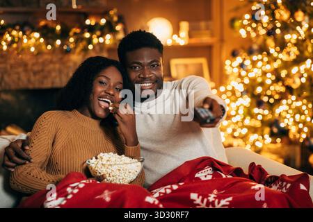 La giovane coppia si diverte con la serata del film di Natale con popcorn nell'accogliente soggiorno Foto Stock