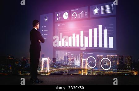 Un uomo d'affari si trova davanti a uno schermo digitale trasparente che mostra le visualizzazioni dei dati rispetto a uno straordinario paesaggio urbano notturno, mettendo in evidenza le prestazioni m Foto Stock