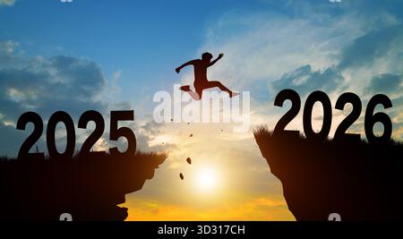 Benvenuti, buon Natale e felice anno nuovo nel 2026. Uomo che salta attraverso la scogliera da 2025 a 2026 con sfondo Sunset e Twilight Sky. Foto Stock