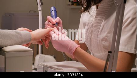 Cura delle unghie. Attrezzo di smontaggio per lucidatura. Manicurista donna che tiene le mani dei clienti utilizzando apparecchiature elettriche automatiche per fare manicure con gel. Foto Stock