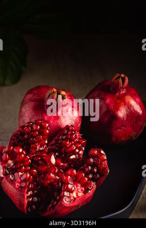 Due melograni interi siedono accanto a uno tagliato aperto, rivelando al suo interno succosi semi rossi. La scena è calda e invitante, perfetta per uno spuntino sano Foto Stock