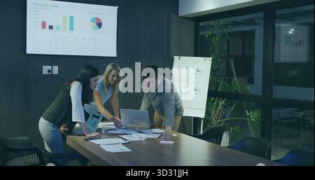 Collaborazione con il team che analizza i grafici, digitando su un notebook argento in ufficio con un display di monitoraggio delle vendite Foto Stock