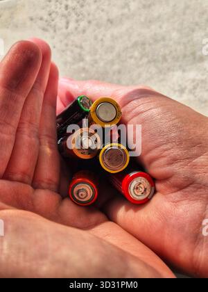 Foto ravvicinata di una mano umana che tiene in mano una manciata di batterie usate e vecchie di varie dimensioni. Foto Stock