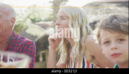 Donna di mezza età che indossa la parte superiore a righe che riposa il mento a portata di mano nel patio illuminato dal sole, con caraffa e occhiali Foto Stock