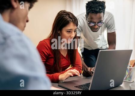 Un giovane team multiculturale, che include un uomo di colore e una donna ispanica, collabora su un notebook in un ambiente di ufficio moderno. Foto Stock