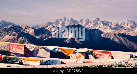 Alba sulle alte montagne innevate e la bandiera buddista tibetana di preghiera. Foto Stock