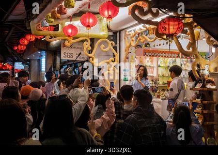 Uno stallholder che vende ocarine dimostra come suonarne uno a forma di gatto al mercato notturno, Jishan Street, Jiufen, Taiwan Foto Stock
