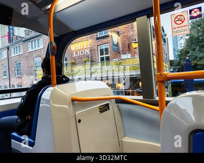 Manchester, Regno Unito - 29 settembre 2025: Passeggero seduto all'interno di un moderno autobus cittadino, edifici in mattoni, cartello vietato fumare visibile all'esterno. Foto Stock