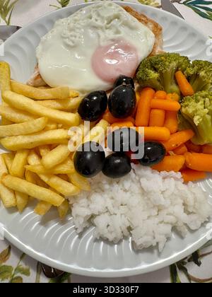 Piatto di cibi assortiti, tra cui uova fritte, pollo, riso, patatine fritte, broccoli, carote e olive nere. Foto Stock