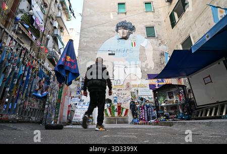 Neapel, Italia. 4 novembre 2025. Un mercante di souvenir passeggia davanti al famoso murale che raffigura Diego Armando Maradona nel "largo Maradona" nei quartieri spagnoli. Il campione del mondo argentino, uno dei migliori calciatori della storia, ha giocato in città sul Vesuvio dal 1984 al 1991 ed è venerato lì come un santo. Maradona morì il 25 novembre 2020. Credito: Arne Dedert/dpa/Alamy Live News Foto Stock
