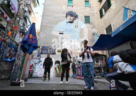 Neapel, Italia. 4 novembre 2025. Un mercante di souvenir passeggia davanti al famoso murale che raffigura Diego Armando Maradona nel "largo Maradona" nei quartieri spagnoli. Il campione del mondo argentino, uno dei migliori calciatori della storia, ha giocato in città sul Vesuvio dal 1984 al 1991 ed è venerato lì come un santo. Maradona morì il 25 novembre 2020. Credito: Arne Dedert/dpa/Alamy Live News Foto Stock