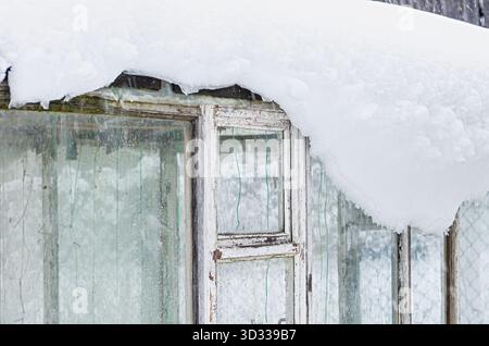 Vecchia serra in legno con finestre in vetro smerigliato sotto spesse nevicate. Veranda rustica in inverno, vetro vintage, clima freddo, dacia, scenario rurale, gar Foto Stock