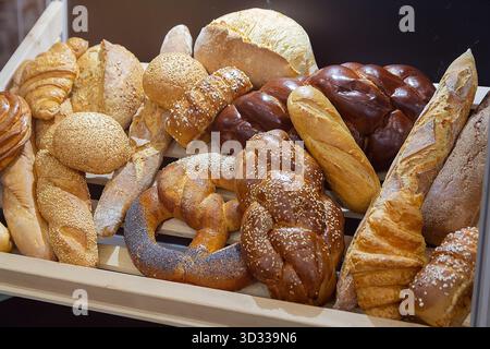 Un bancone da forno con una vasta gamma di panini, panini e baguette. Un'illuminazione calda e luminosa mette in risalto la freschezza. Foto Stock