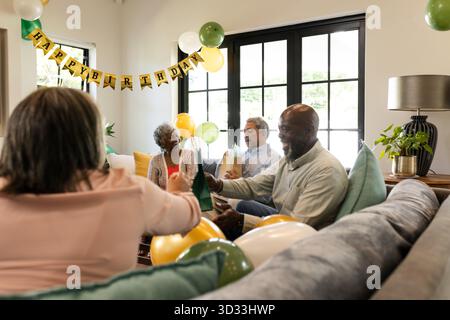 Festeggiamo il compleanno a casa, un gruppo variegato che si diverte a bere e ridere insieme. Celebrazione, festa, multiculturale, amici, riunione, felicità || modello rilasciato Foto Stock