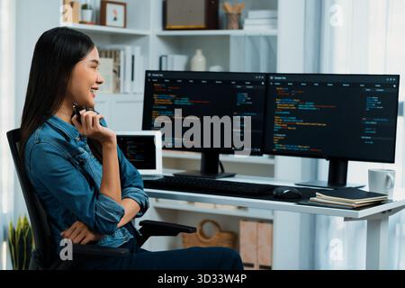 Giovane sviluppatore di IT asiatico che cerca informazioni online su pc per una bella posa con i dati del programma di codifica dell'applicazione del sito web, indossando una camicia di jeans Foto Stock