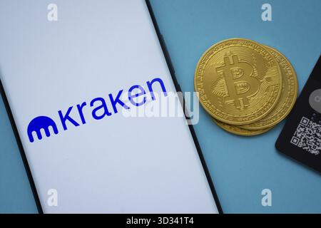 Dacca, Bangladesh- 26 agosto 2025: Smartphone con logo Kraken circondato da monete Bitcoin e carte di pagamento Foto Stock
