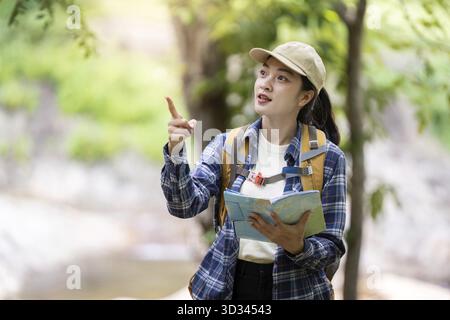 Una giovane donna con uno zaino esamina una mappa mentre esplora una foresta lussureggiante. Concetto di avventura e navigazione all'aperto Foto Stock