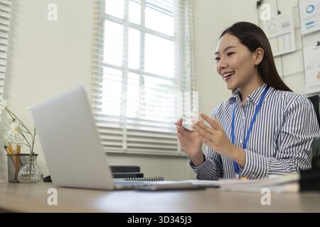 Una donna d'affari sorridente partecipa a una videochiamata, mostrando comunicazioni efficaci e dinamiche di lavoro a distanza in un ufficio moderno Foto Stock
