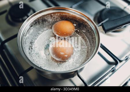 Pentola in acciaio inossidabile con due uova bollenti, colazione in acqua con vista dall'alto su una stufa a gas Foto Stock