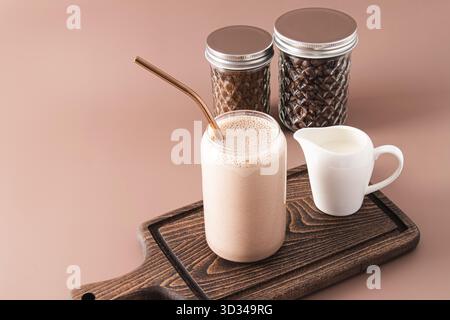 Frullato o caffè appena fatto con latte in un moderno bicchiere a forma di barattolo di birra su un tagliere di legno. Vista frontale Foto Stock