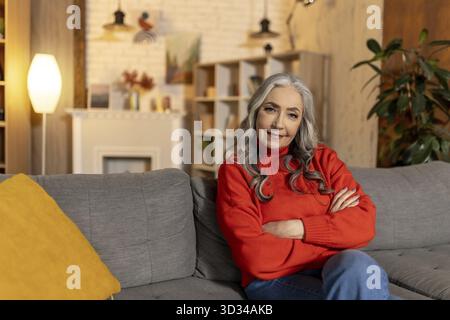 A casa. Bella donna anziana dai capelli lunghi seduta sul divano a casa Foto Stock