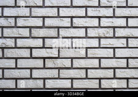 Cuciture in mattoni bianchi e grigi scuri, muratura in pietra chiara. Piastrelle della facciata Foto Stock