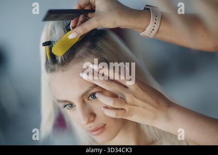 Parrucchiere femmina che fa estensioni di capelli a giovane donna con capelli biondi in salone di bellezza. Prolunga professionale per capelli Foto Stock