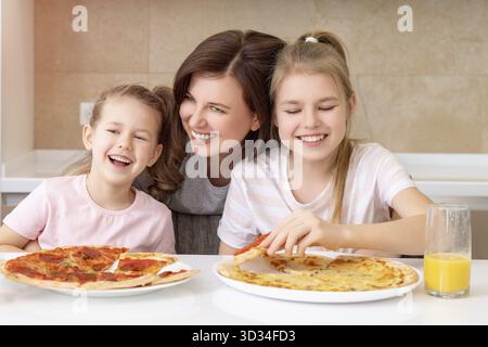 Madre e due figlie mangiano pizza fatta in casa ad un tavolo in cucina Foto Stock