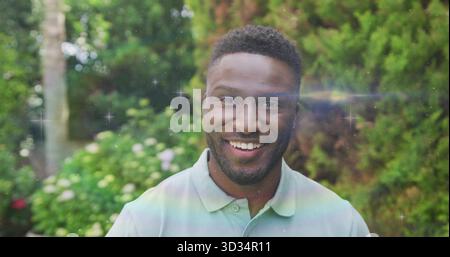 Uomo sorridente in piedi in giardino privato, con lenti da sogno e fogliame verde Foto Stock