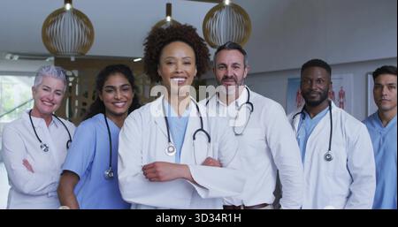 Sei persone in piedi nel corridoio dell'ospedale con cappotti bianchi, scrub blu, stetoscopi, grafico di anatomia Foto Stock