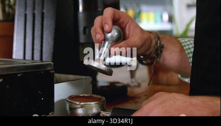 Barista in camicia a quadri con manomissione sul portafiltro presso la postazione espresso con macchie di caffè, copia spazio Foto Stock