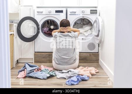 Giovane donna triste e stanca seduta in lavanderia Foto Stock