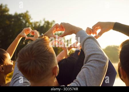 Persone che fanno gesti cardiaci con le dita al sole, vista posteriore della folla di giovani amici felici Foto Stock